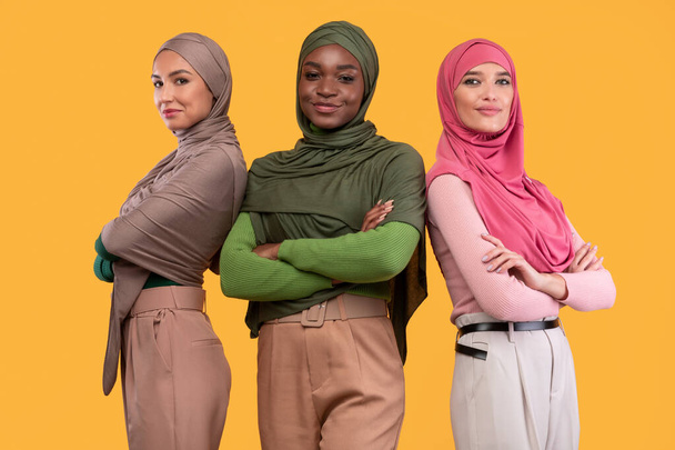 Três mulheres muçulmanas bem sucedidas no Hijab em pé sobre fundo amarelo - Foto, Imagem