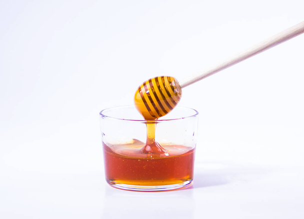 Мед со стеклянной медовой ковшом в стеклянной чаше на белом фоне - Фото, изображение