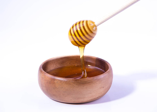 Honey with wooden honey dipper in wooden bowl on white background - Fotoğraf, Görsel