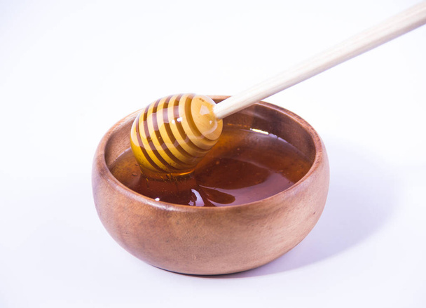 Honing met houten honingdipper in houten kom op witte ondergrond - Foto, afbeelding