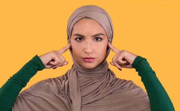 Muslim Lady Cubriendo Orejas No Escuchando a Otros Opiniones, Fondo Amarillo - Foto, imagen