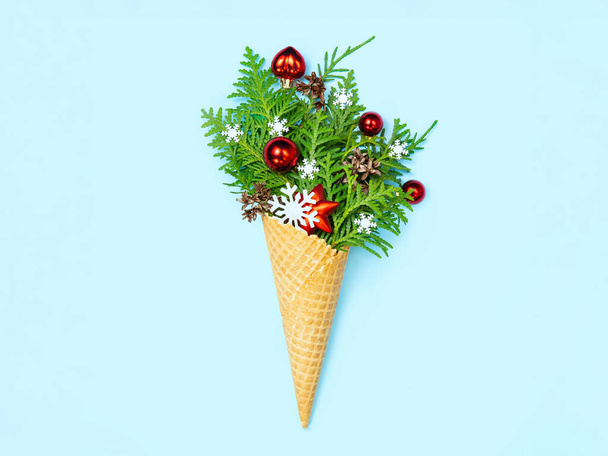 Ice cream cone with thuja sprigs and Christmas toys. Blue background. New Year card. Copy space, flat lay. The concept photo is an original Christmas present. - Photo, Image