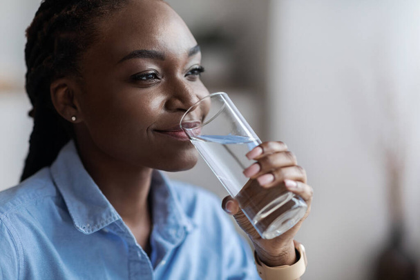 Idratazione. Bella donna nera che beve acqua minerale dal vetro, colpo di primo piano - Foto, immagini