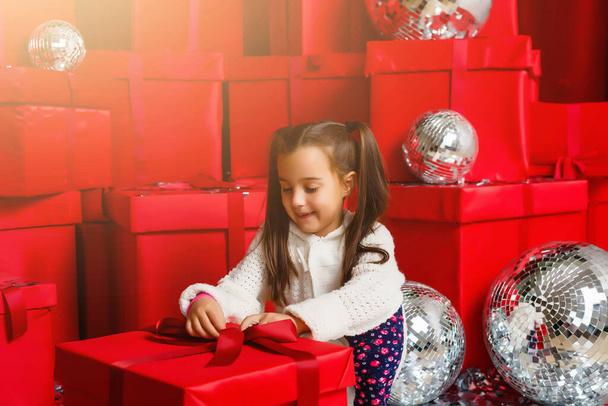 Χαρούμενο χαριτωμένο κοριτσάκι με δώρο. Το κοριτσάκι είναι ανάμεσα στα Χριστουγεννιάτικα δώρα.. - Φωτογραφία, εικόνα