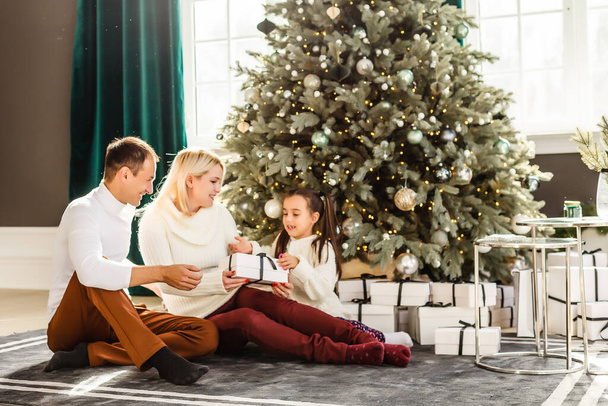 Family with gifts in front of Christmas tree - Foto, afbeelding