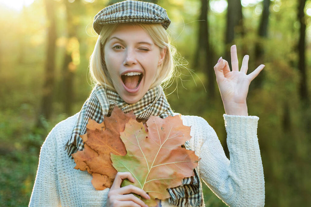 Autumn woman. Happy autumn girl wink. Cheerful carefree autumn woman in park on sunny day. Girl playing with leaves on autumn leaves background. - 写真・画像