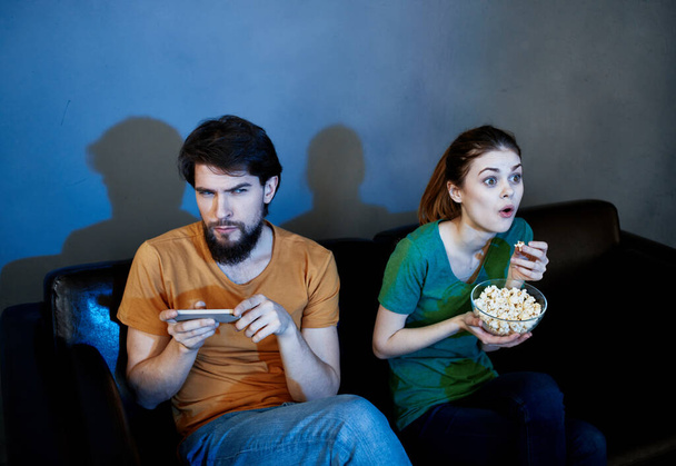 Férfi és nő a bőrkanapén popcornnal tévézni esténként - Fotó, kép
