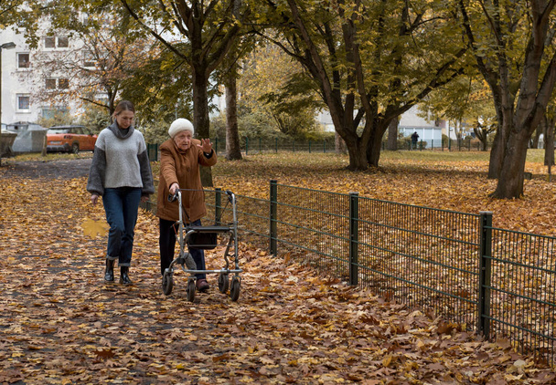 Mujer mayor dando un paseo con su nieta con la ayuda de un caminante en invierno - Foto, Imagen