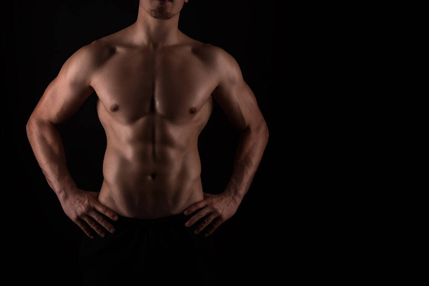 Handsome young bodybuilder with muscular back standing on black background - Fotoğraf, Görsel