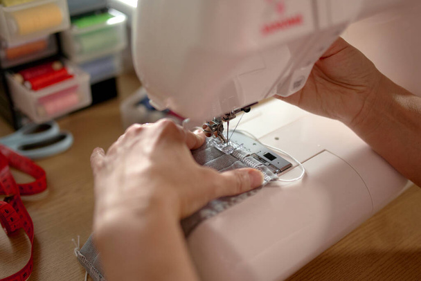 Manos de mujer usando la máquina de coser para coser la mascarilla para la pandemia covid corona - Foto, imagen