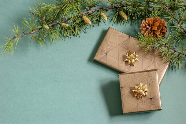 Rama de árbol de Navidad, cono y regalos empacados en el fondo verde. Cajas de embalaje hechas a mano, concepto Diy.  - Foto, Imagen