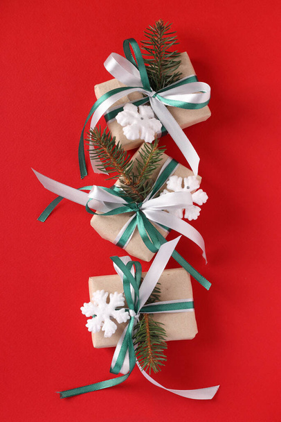 Three Christmas giftboxs with green and white ribbon on red surface. Holiday card. Top view. Vertical format - Photo, Image
