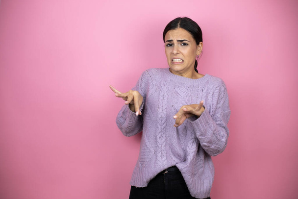Bella donna che indossa un maglione viola casual su sfondo rosa espressione disgustata, dispiaciuto e timoroso facendo faccia disgusto perché reazione di avversione. Concetto irritante - Foto, immagini