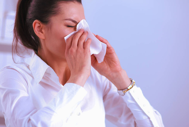 Young businesswoman blowing her nose, sits at the desk - Photo, image