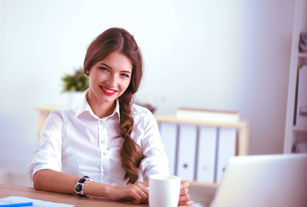 Attractive businesswoman sitting on desk in the office - 写真・画像