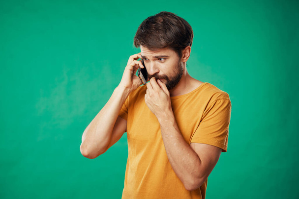  sárga pólós férfi, zöld háttérrel, telefonon beszél. - Fotó, kép