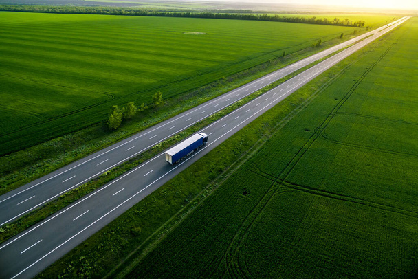 camión azul conduciendo por carretera asfaltada a lo largo de los campos verdes. visto desde el aire. Paisaje vista aérea. fotografía de drones. entrega de carga  - Foto, Imagen