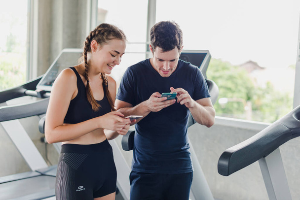 Couples exercise at the gym. Couple having fun playing with smartphones Near the exercise machine. - Φωτογραφία, εικόνα