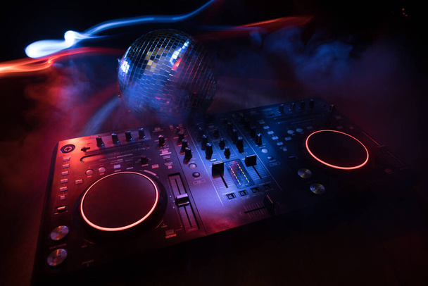 Σύλλογος μουσική έννοια. DJ κονσόλα deejay-mixing γραφείο στο σκοτάδι με πολύχρωμο φως. Mixer ψυχαγωγίας εξοπλισμού DJ σταθμό. Επιλεκτική εστίαση - Φωτογραφία, εικόνα