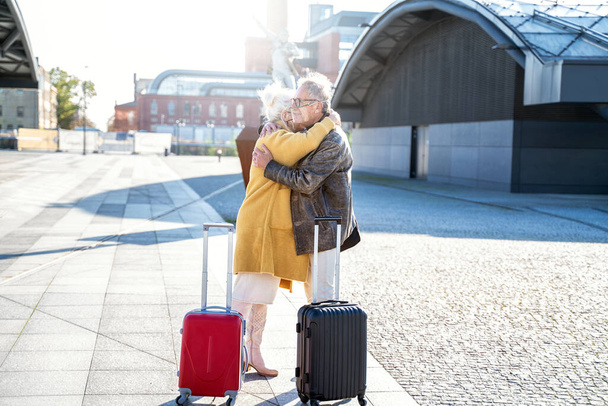 Seniors couple saying goodbye or hello to each other on the train station. Two mature people wearing protective mask, hugging. Travel and relationship concept during a pandemic. Outdoor photo. - Φωτογραφία, εικόνα