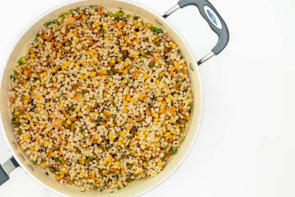 Un mélange salé de couscous perlé, orzo, haricots garbanzo bébé, et le quinoa rouge fermer sur la poêle sur fond blanc, plat étendre avec un espace de copie - Photo, image
