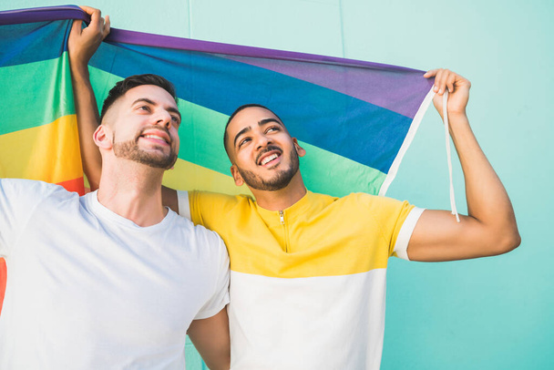 Gay couple embracing and showing their love with rainbow flag. - Fotó, kép