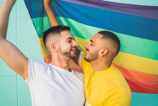 Gay couple embracing and showing their love with rainbow flag. - Foto, afbeelding