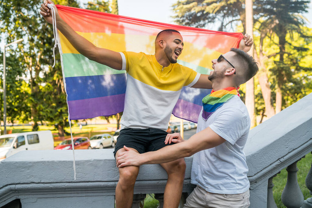Gay couple embracing and showing their love with rainbow flag. - Фото, изображение