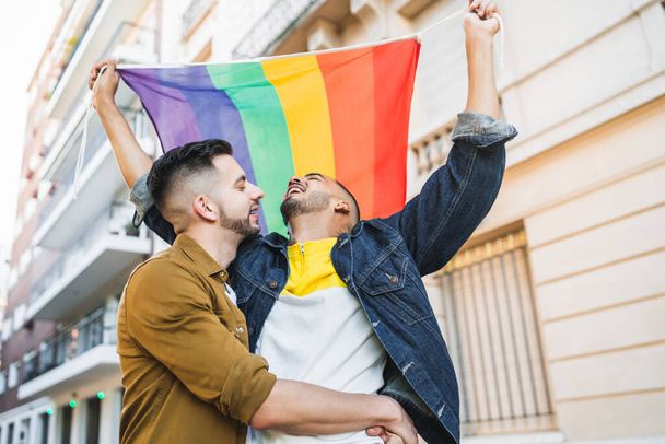 Gay couple embracing and showing their love with rainbow flag. - Photo, Image
