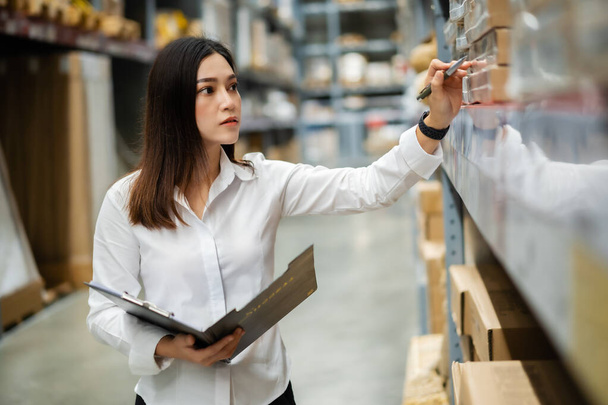 young woman worker holding clipboard and checking inventory in the warehouse store - Foto, imagen