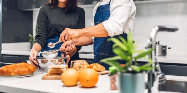 Νεαρό οικογενειακό ζευγάρι που διασκεδάζει μαγειρεύοντας μαζί με μπισκότα ψησίματος και συστατικά κέικ στο τραπέζι.Ευτυχισμένο ζευγάρι που ψάχνει να προετοιμάσει τη ζύμη στην κουζίνα - Φωτογραφία, εικόνα