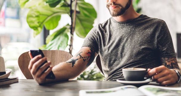 Handsome hipster man relaxing using digital smartphone with coffee and looking at screen typing message at table in cafe and restaurant,playing game online and social media - Photo, Image