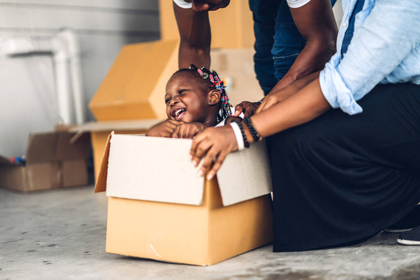 Portret van genieten van gelukkige liefde zwarte familie afrikaanse Amerikaanse vader en moeder met weinig afrikaanse meisje glimlachen zitten in kartonnen doos bij nieuw huis uitpakken tijdens het verplaatsen en hebben leuke momenten goede tijd - Foto, afbeelding