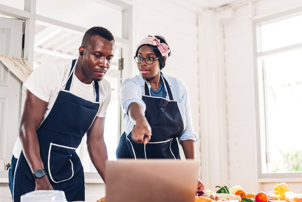 Porträt der Liebe afrikanisch-amerikanisches Paar, das Spaß am gemeinsamen Kochen hat und im Internet mit Laptop nach Rezepten sucht, um das leckere Essen in der heimischen Küche zuzubereiten - Foto, Bild