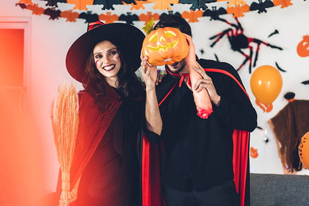 Paar, das Spaß dabei hat, Kürbisse in den Händen zu halten und Karnevalskostüme und Make-up mit Fledermäusen und Luftballons auf dem Hintergrund bei der Halloween-Party zu tragen.Halloween-Feiertagskonzept - Foto, Bild