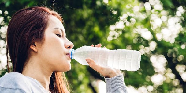Женщина пьет воду из бутылки, расслабляясь и чувствуя себя свежей на зеленом природном фоне в летнем зеленом парке. Понятие здорового образа жизни - Фото, изображение