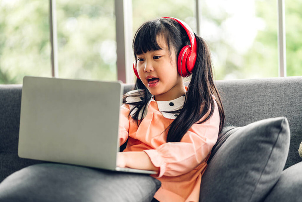 Okul çocuğu küçük kız öğreniyor ve dizüstü bilgisayara bakıyor ev ödevi yapıyor çevrimiçi eğitim sistemi ile bilgi öğreniyor. Evde öğretmenle çocuk video konferansı - Fotoğraf, Görsel