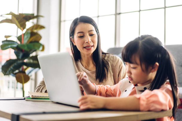 Matka i azjatyckie dziecko mała dziewczynka uczenia się i patrząc na laptopa podejmowania pracy domowej studiuje wiedzę z edukacji online e-learning system.children wideokonferencja z nauczycielem nauczycielem w domu - Zdjęcie, obraz