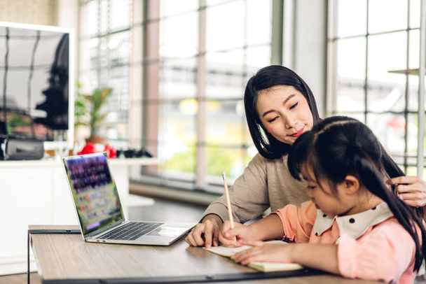 Мама с ребенком маленькая девочка учится и смотрит на ноутбук, делая домашнее задание, изучая знания с помощью системы онлайн-образования e-learning. - Фото, изображение