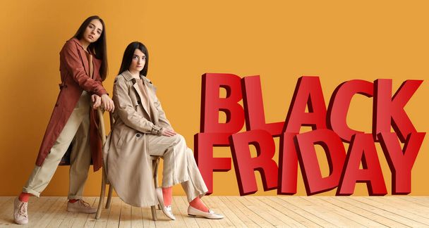 Stilvolle junge Frauen in der Nähe der Farbwand mit Text BLACK FRIDAY - Foto, Bild
