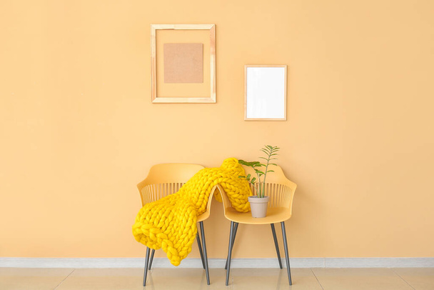 Židle s pletenými kostkami a pokojovou rostlinou v blízkosti barevné stěny - Fotografie, Obrázek
