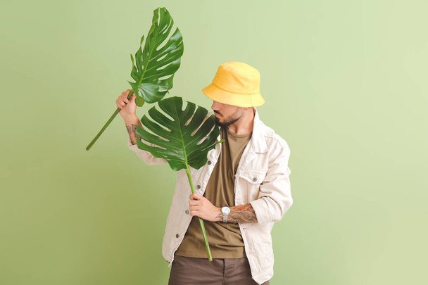 Módní mladý muž s tropickými listy na barevném pozadí - Fotografie, Obrázek