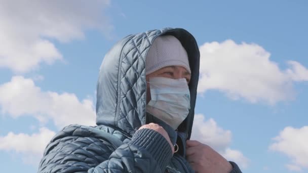 Οι άνθρωποι που φοβούνται την πανδημία φορούν προστατευτική μάσκα στους δρόμους. επικίνδυνη μόλυνση covid-19. μια γυναίκα με κουκούλα έξω με ιατρική μάσκα. Υγεία, καραντίνα από κορωνοϊό. προστασία από λοιμώξεις - Πλάνα, βίντεο