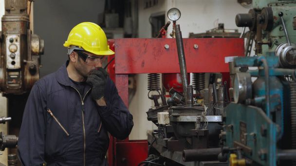 Trabajador de fábrica hablando por radio portátil mientras inspecciona piezas de maquinaria - Foto, imagen