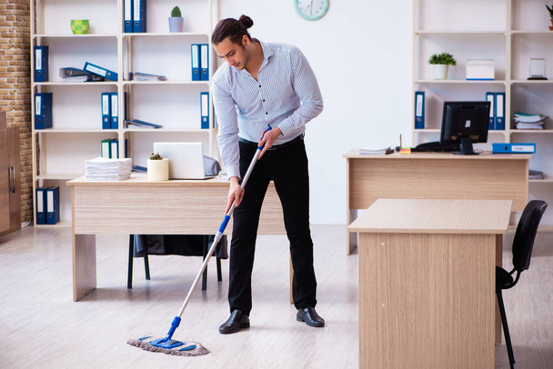 Jonge mannelijke werknemer schoonmaak kantoor tijdens pandemie - Foto, afbeelding