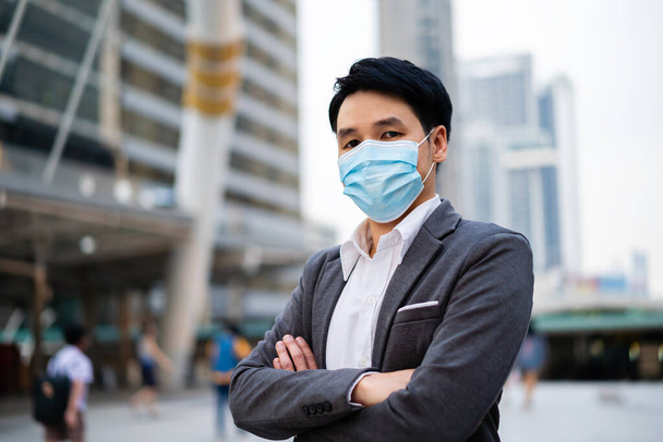 business man with arms crossed and wearing medical mask during coronavirus (covid-19) pandemic in the city - Valokuva, kuva