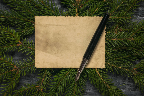 Caneta-tinteiro preta em um pedaço de papel velho contra o fundo de ramos de abeto. - Foto, Imagem