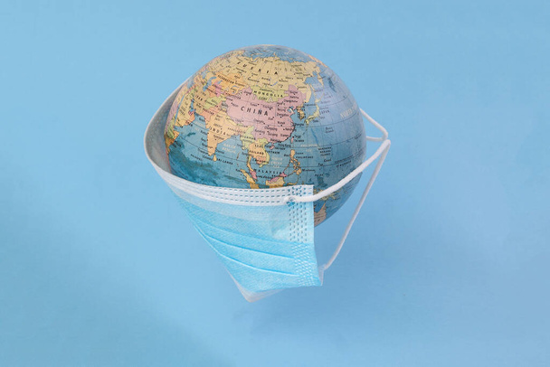 globo planeta mapa del mundo tierra usando máscara facial sobre fondo azul - Foto, imagen