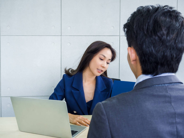 Asian business woman and businessman working together in office. Female boss and young male employee wearing suit open and looking at document blue  folder with laptop computer on desk. - Photo, Image