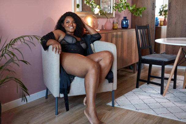 goed uitziende Afrikaanse vrouw met half naakt plus size lichaam zit op fauteuil - Foto, afbeelding